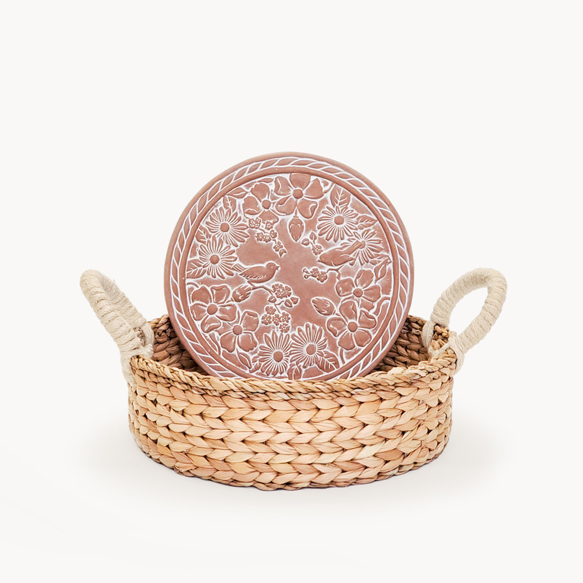 Decorative terracotta plate with floral patterns in a woven basket on a white background