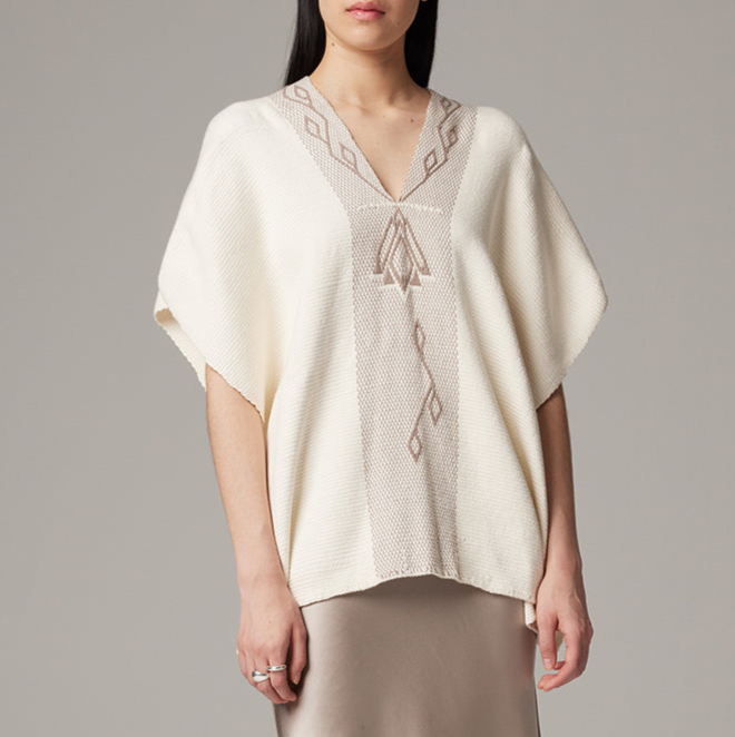 Woman wearing a cream-colored poncho with intricate patterns on a gray background