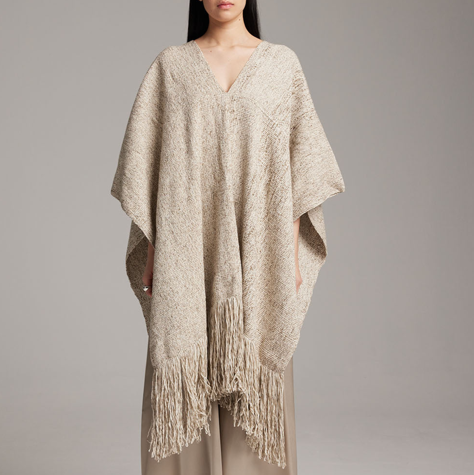 Beige poncho with fringe details on a plain background