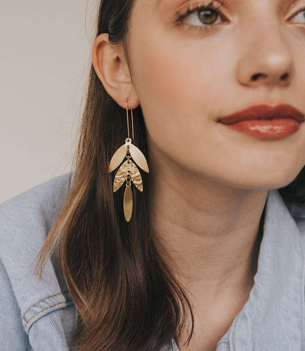 Close-up of a woman wearing gold leaf-shaped earrings with a neutral background
