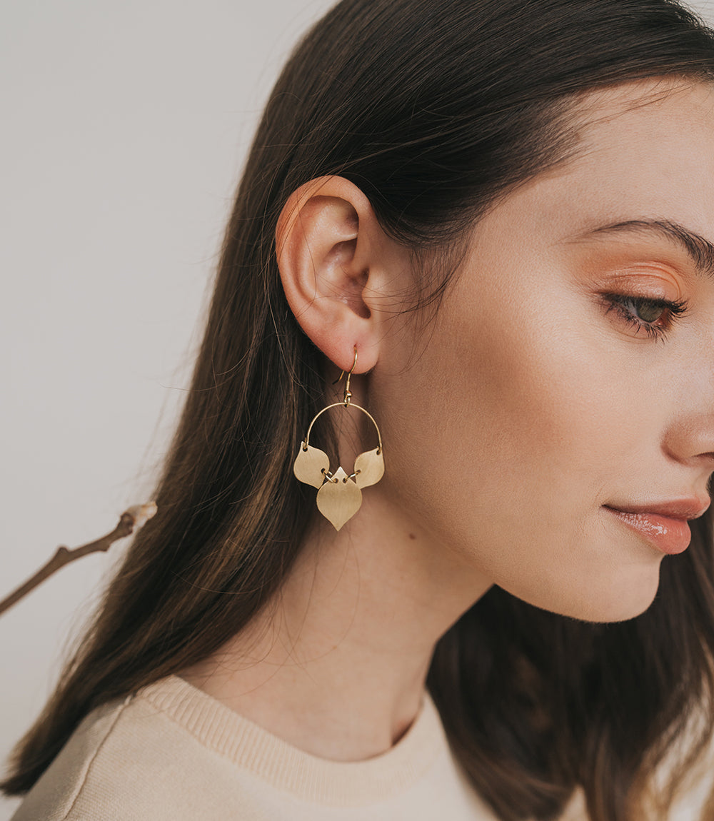 Close-up of a woman wearing gold hoop earrings with a neutral background