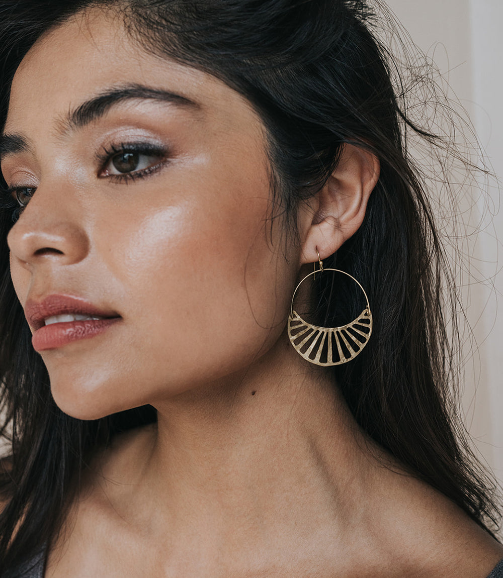 Close-up of a woman wearing a gold hoop earring with a neutral background