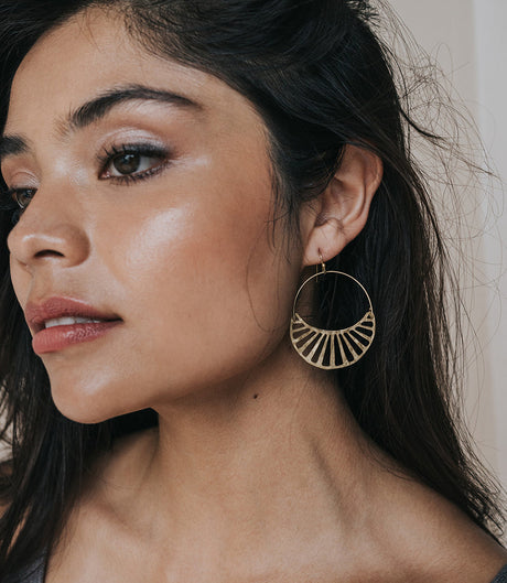 Close-up of a woman wearing a gold hoop earring with a neutral background