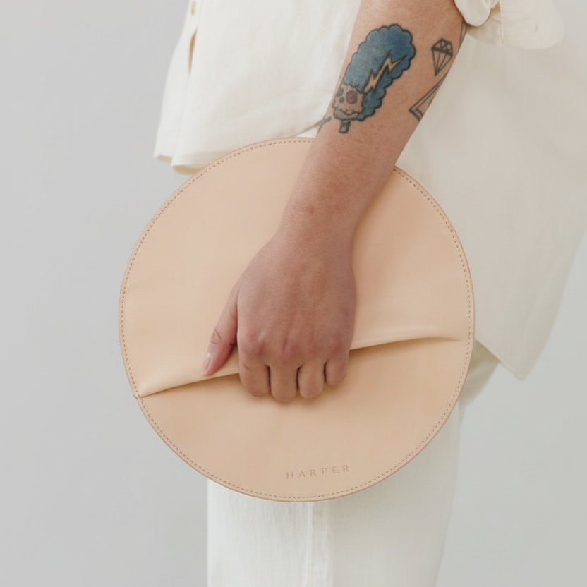 Person holding a beige circular clutch bag against a plain background