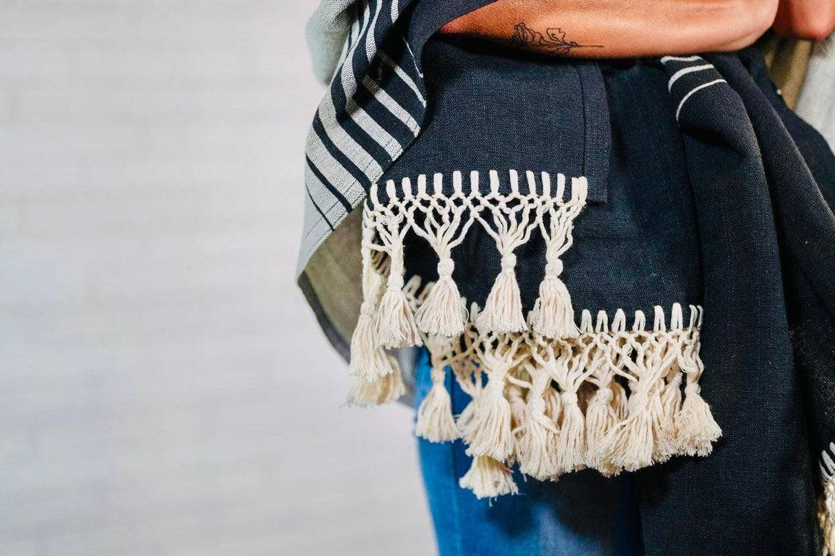 Close-up of a dark blue garment with white macramé fringe against a plain background
