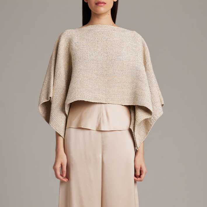 Woman wearing a beige poncho over a matching outfit against a plain background