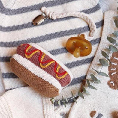 Knitted hot dog toy with mustard on a striped fabric background