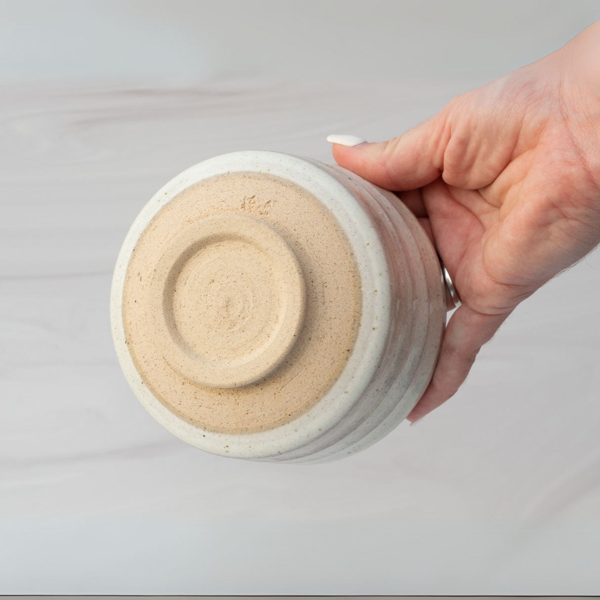 A hand elegantly holds a Beige Ceramic Matcha Bowl upside down, showcasing its rounded base, reminiscent of Minoyaki pottery and ideal as a matcha accessory.