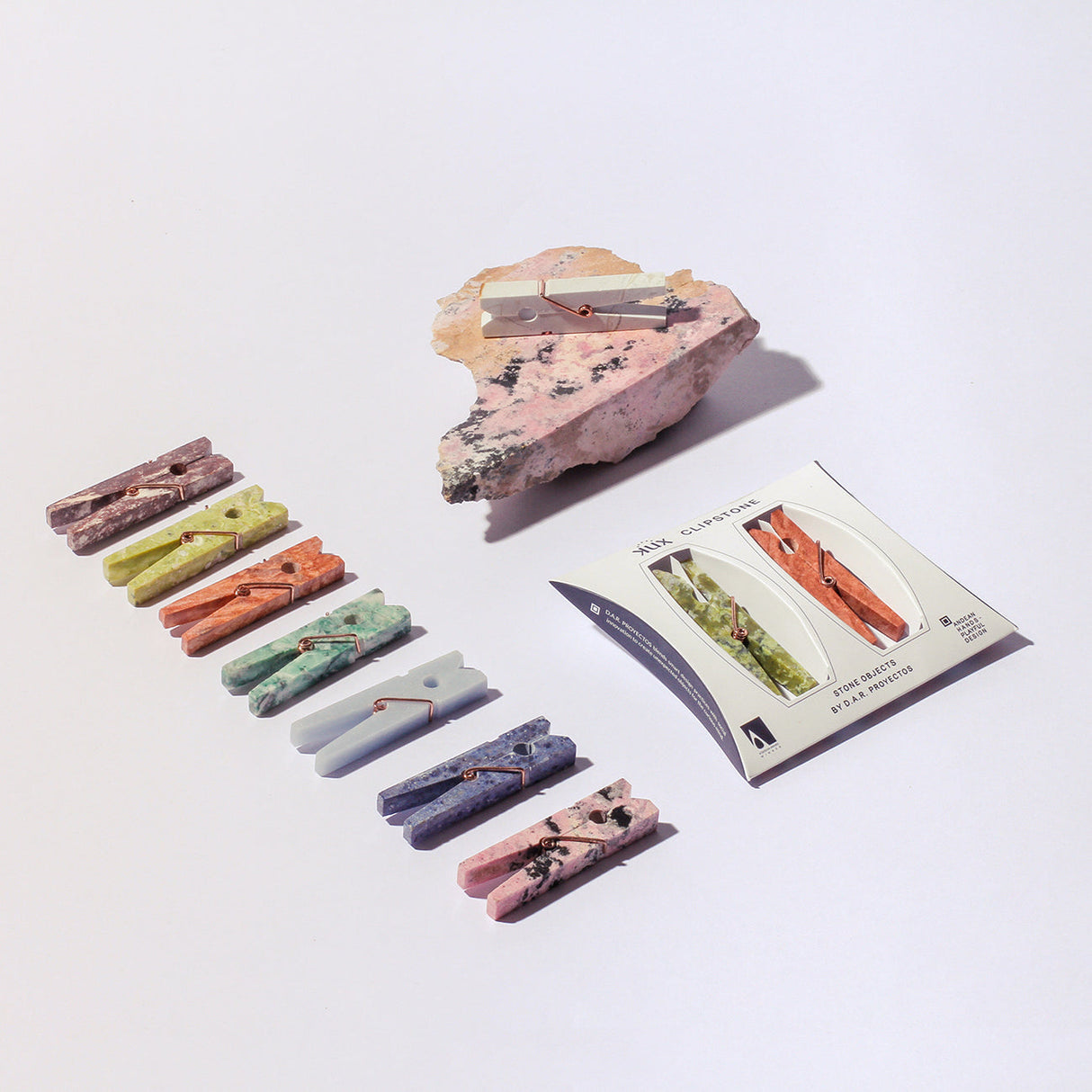Set of colorful stone clothespins on a white background with a rock and card.