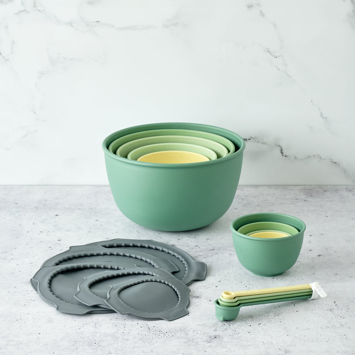 Set of green and gray nesting bowls and measuring cups on a light gray surface.