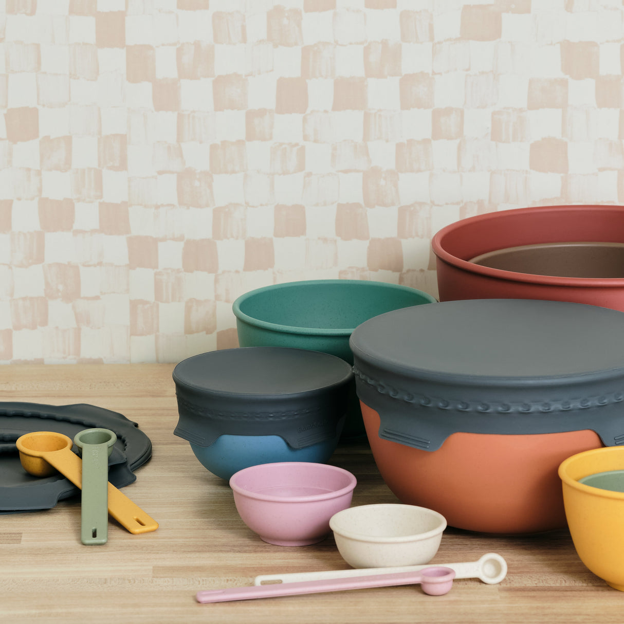 Set of colorful silicone kitchenware on a wooden surface with a checkered wall background