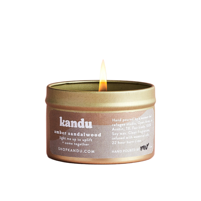Kandu amber sandalwood candle in a tin with a lit flame on a pink background