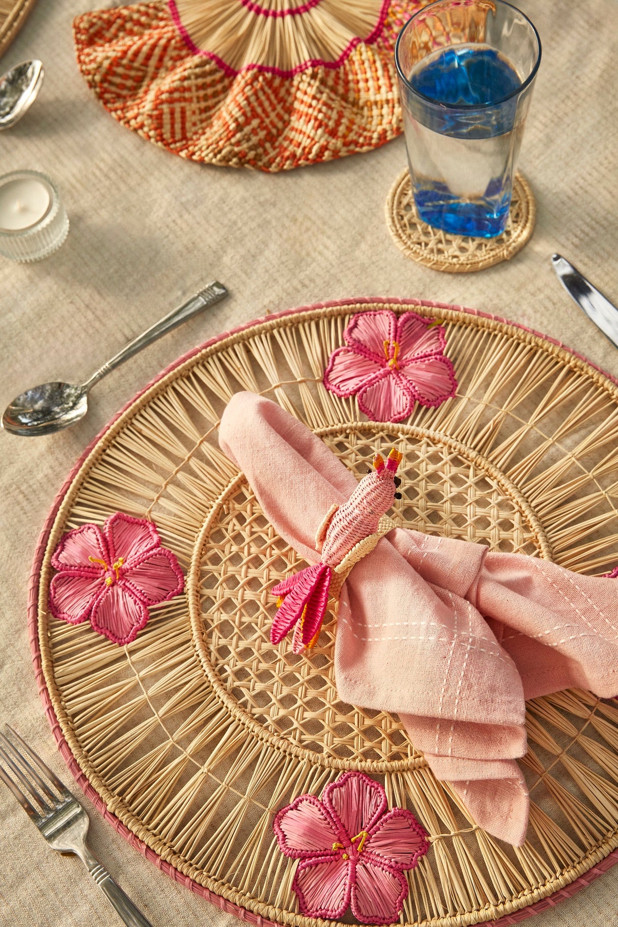 Woven placemat with pink flowers and a folded napkin on a table setting.