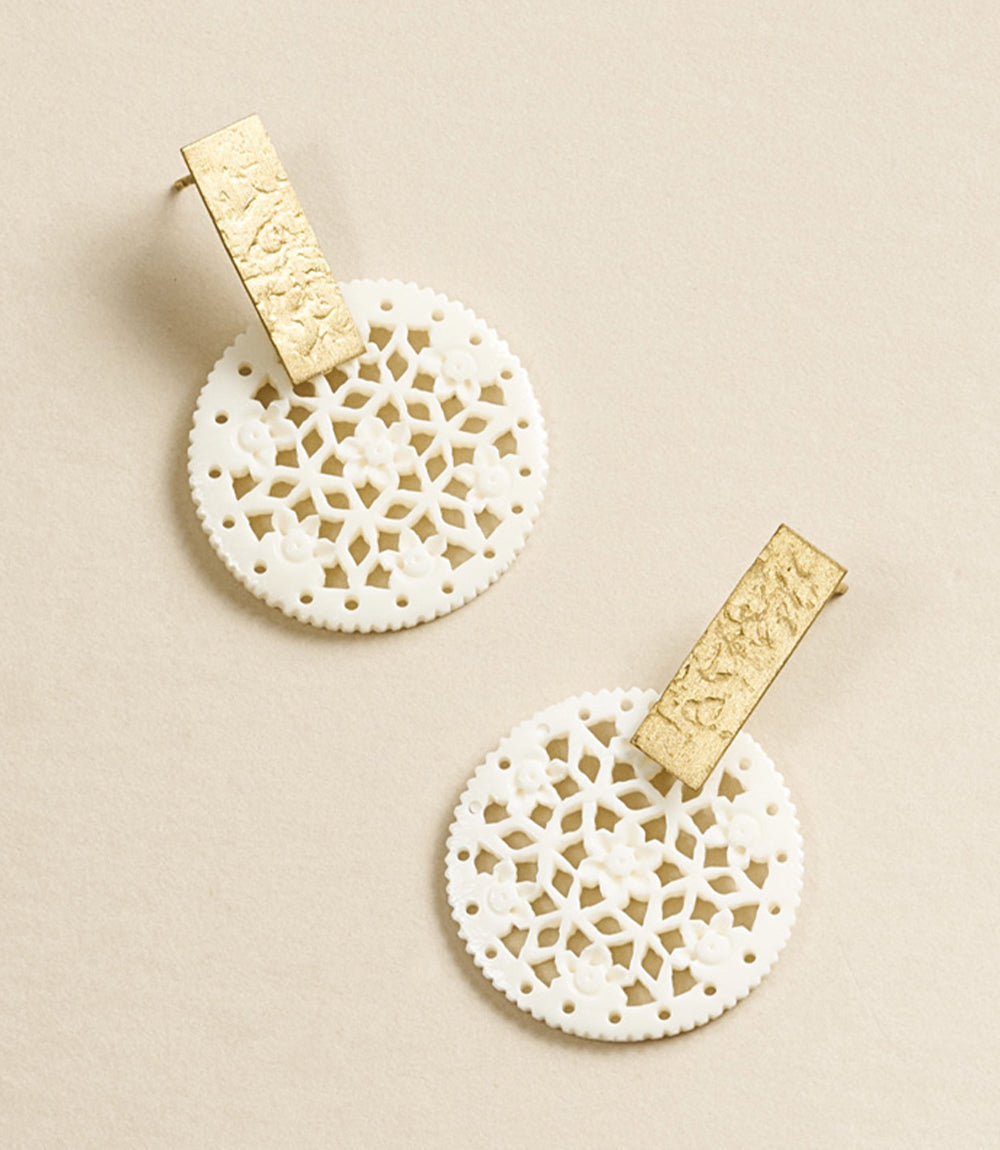 Pair of earrings with gold and white lace-like designs on a beige background