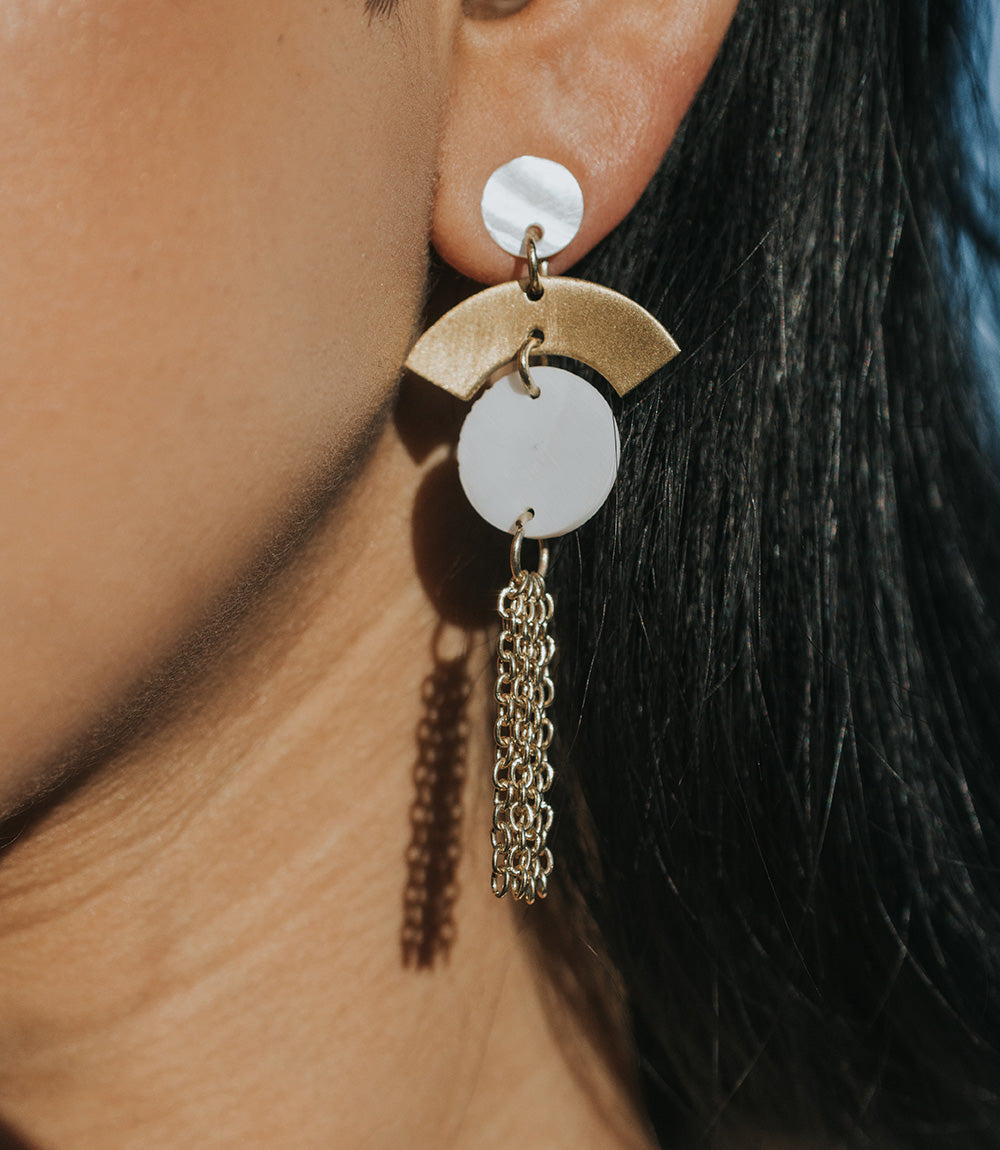 Close-up of a gold and white earring on an ear with dark hair.