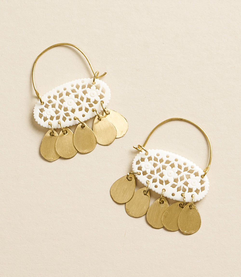Pair of gold hoop earrings with white lace-like centers and gold disc pendants on a beige background.