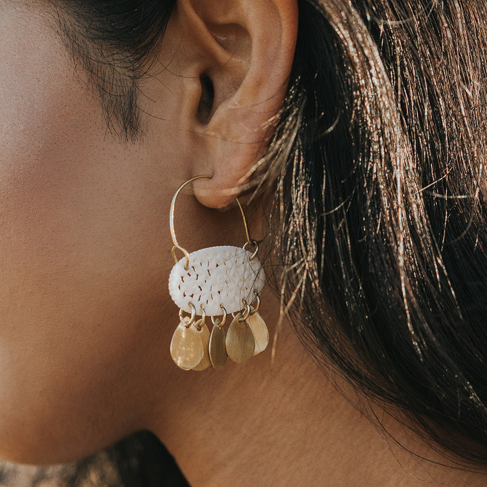Close-up of an ear wearing a gold hoop earring with white ceramic and gold disc charms.