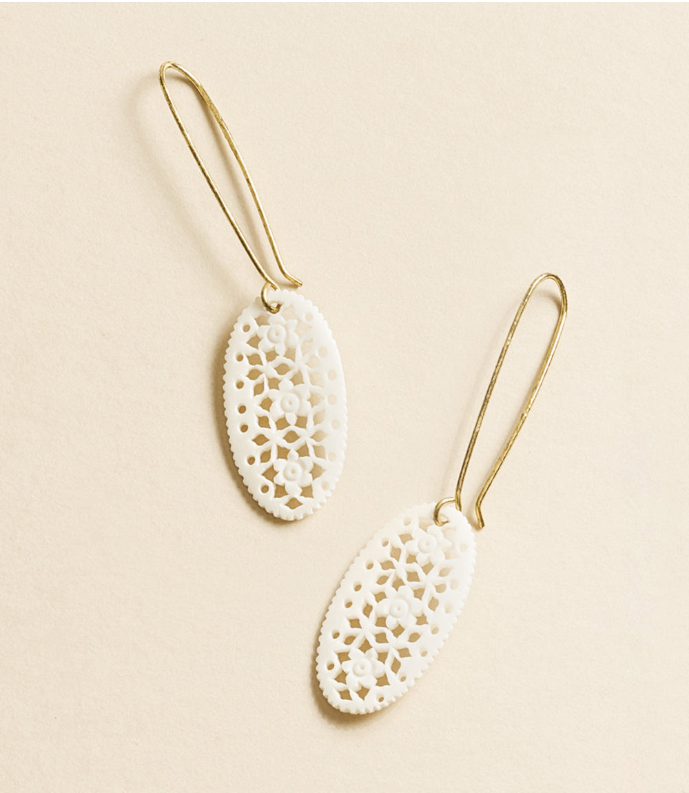 Pair of white lace-like earrings on a beige background