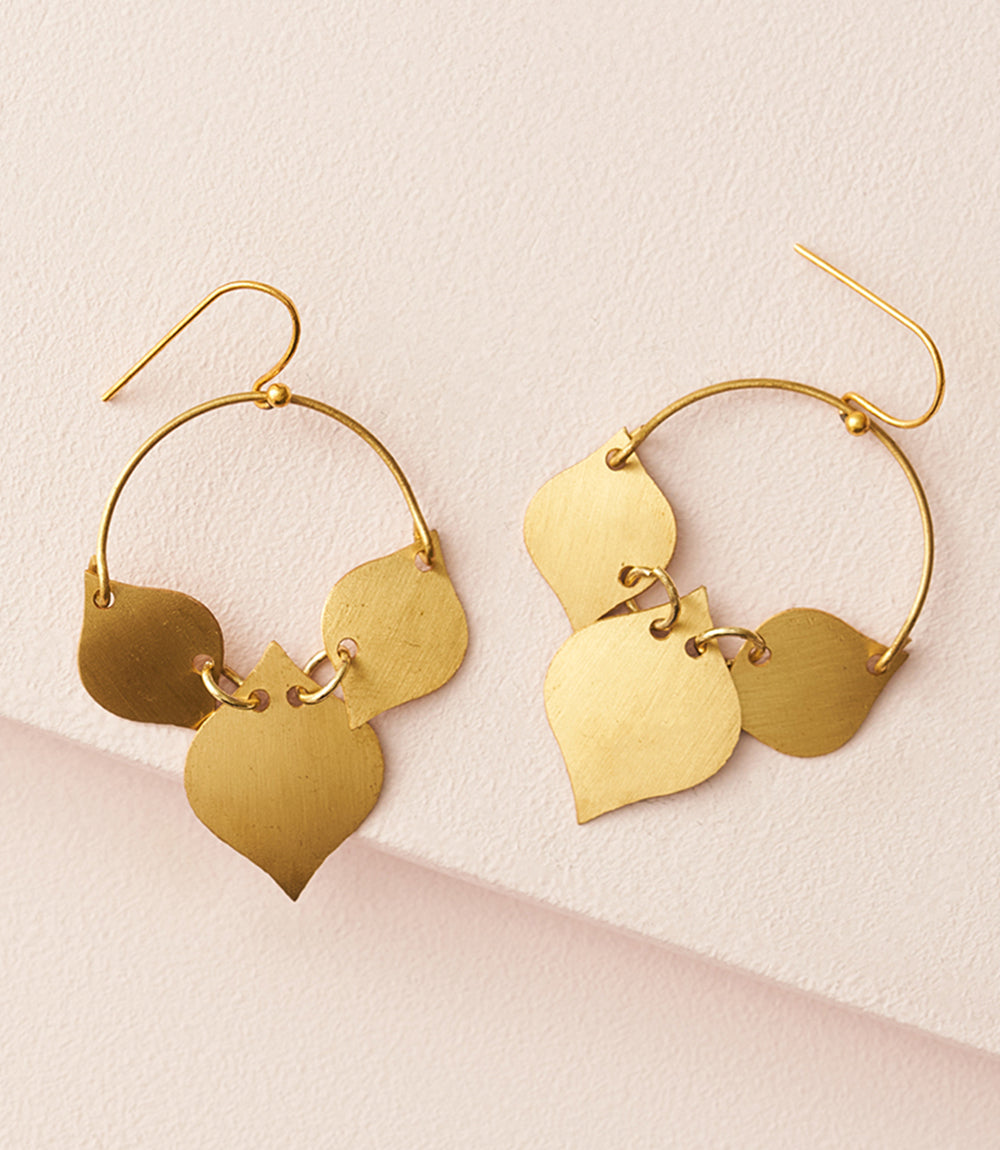 Gold hoop earrings with leaf-shaped pendants on a light pink background