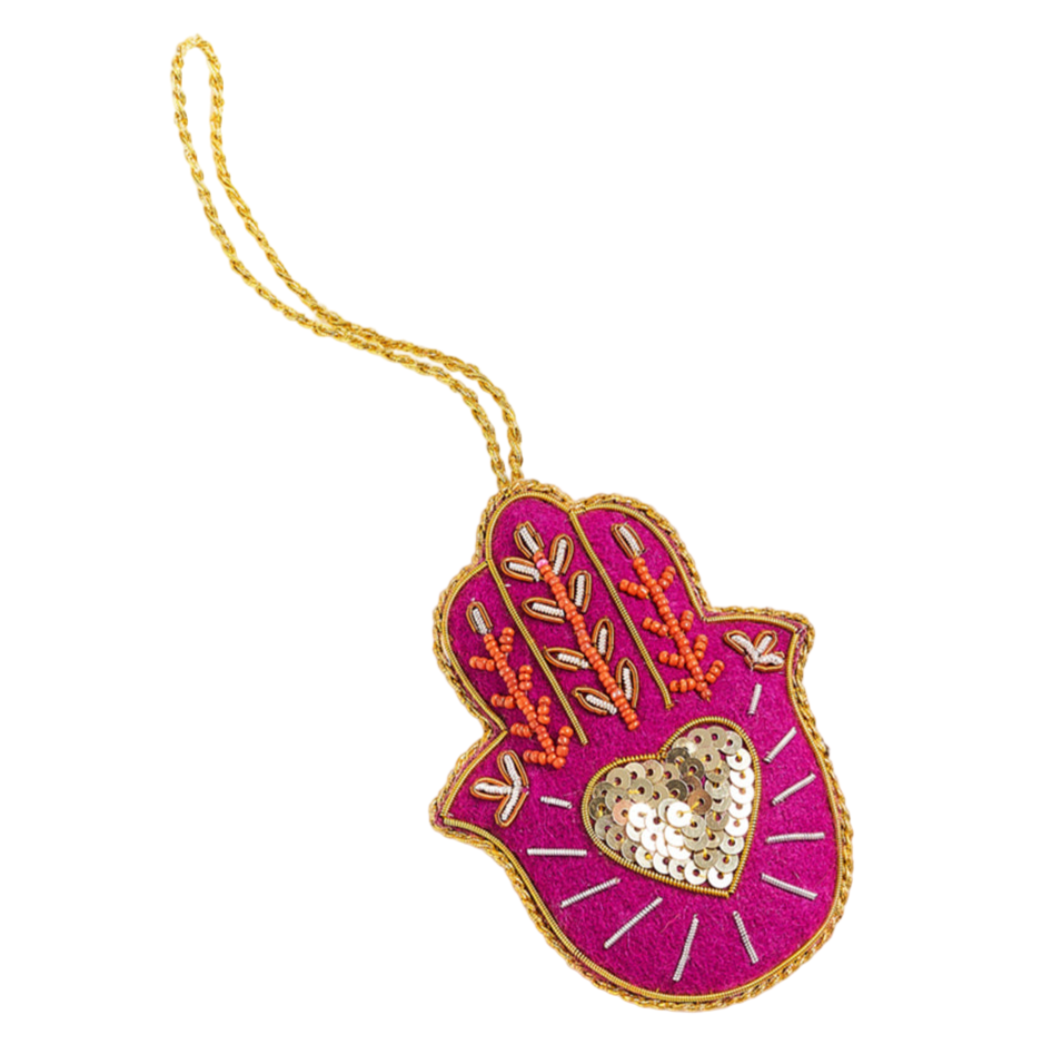 Decorative hamsa hand ornament with pink border and gold heart on a white background