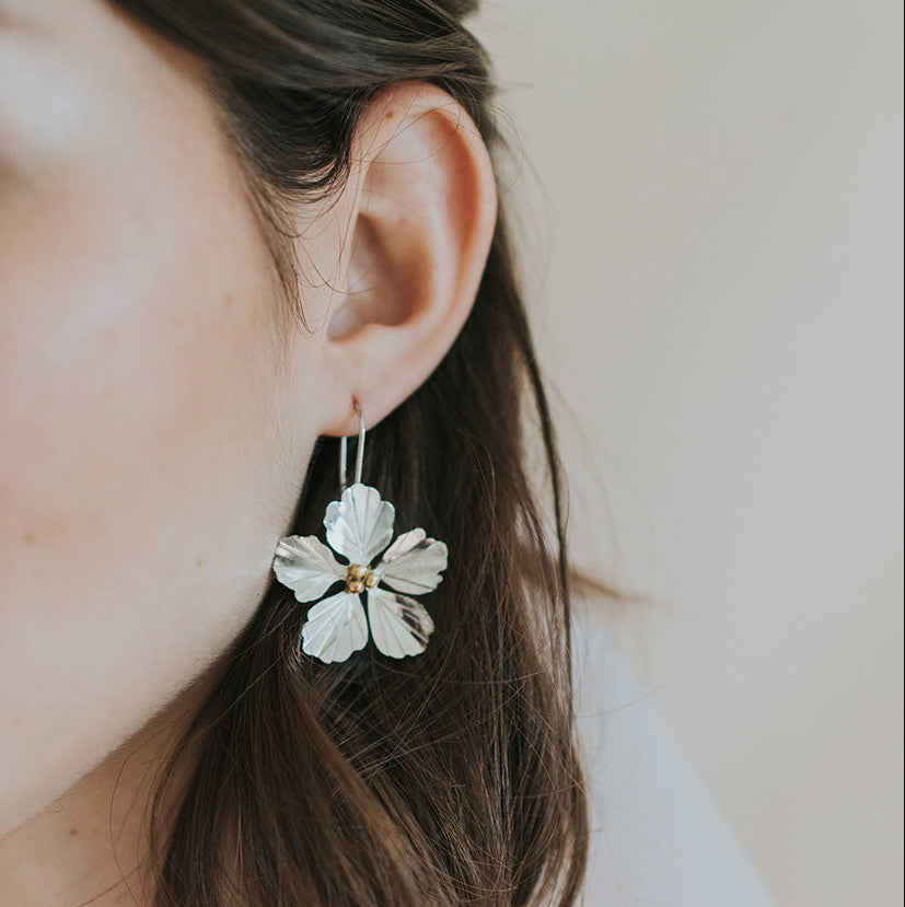 Close-up of a person wearing a floral earring with a neutral background