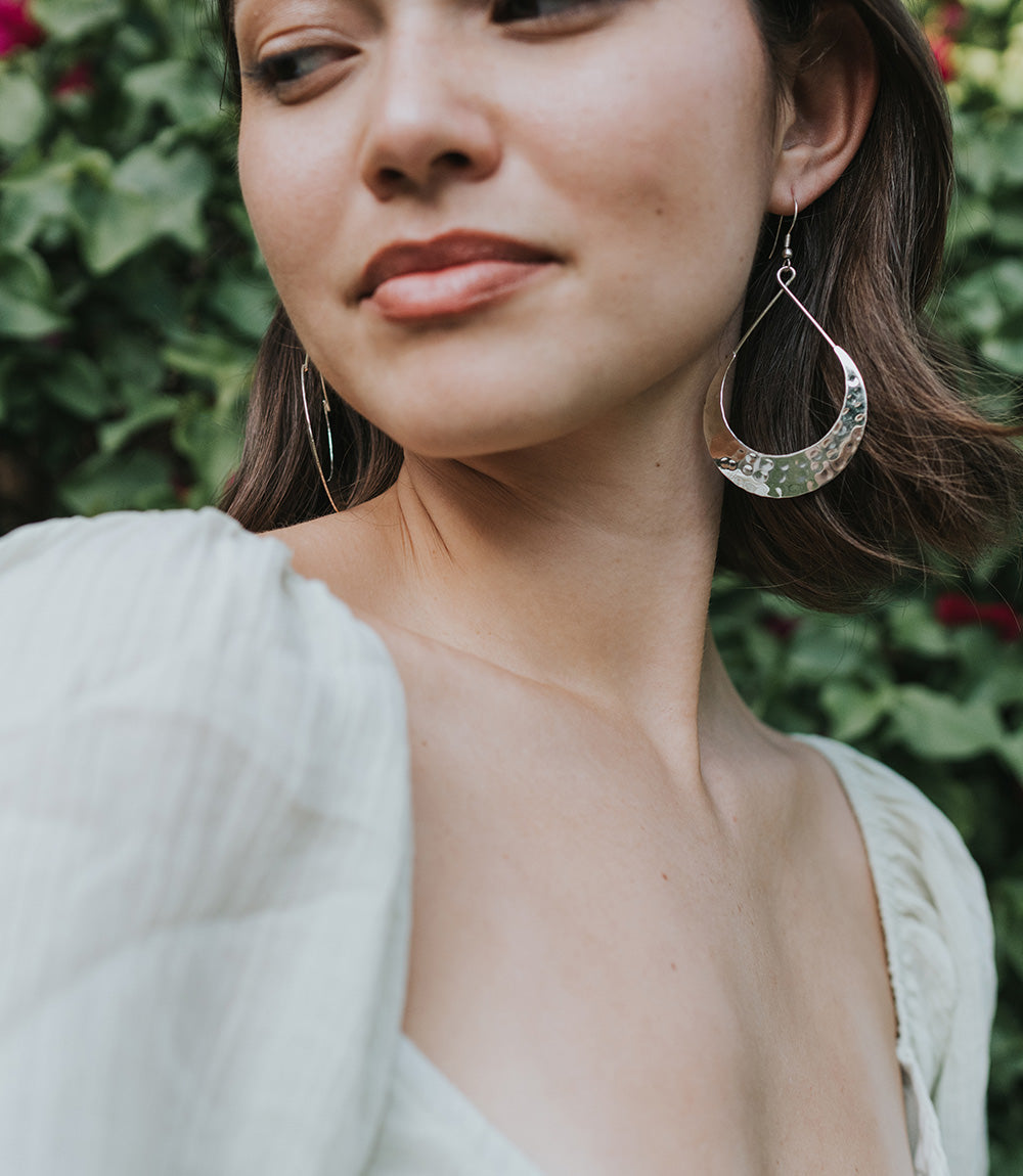 Close-up of a woman wearing silver hoop earrings with a blurred green background