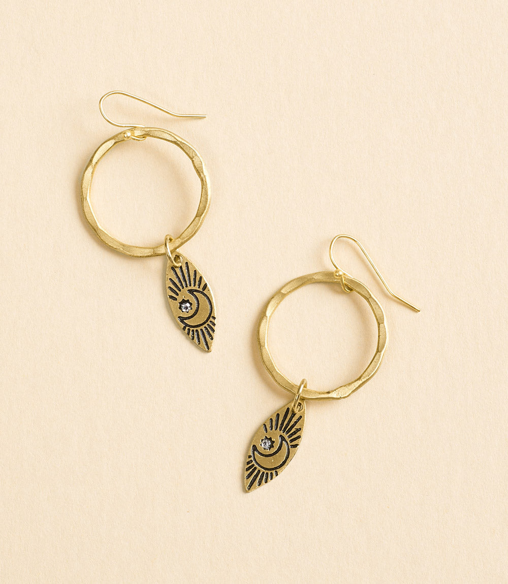 Gold hoop earrings with eye-shaped charms on a beige background
