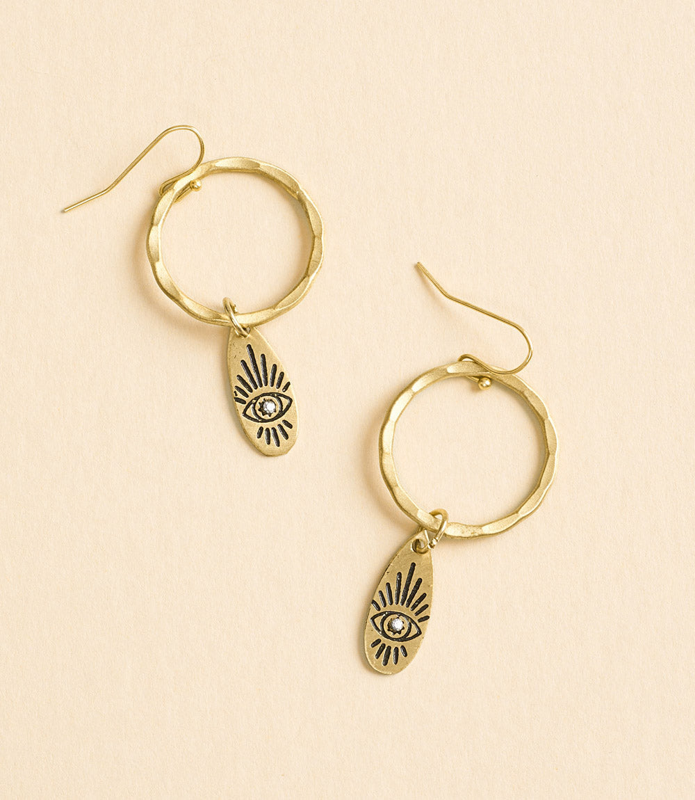 Gold hoop earrings with eye-shaped charms on a beige background