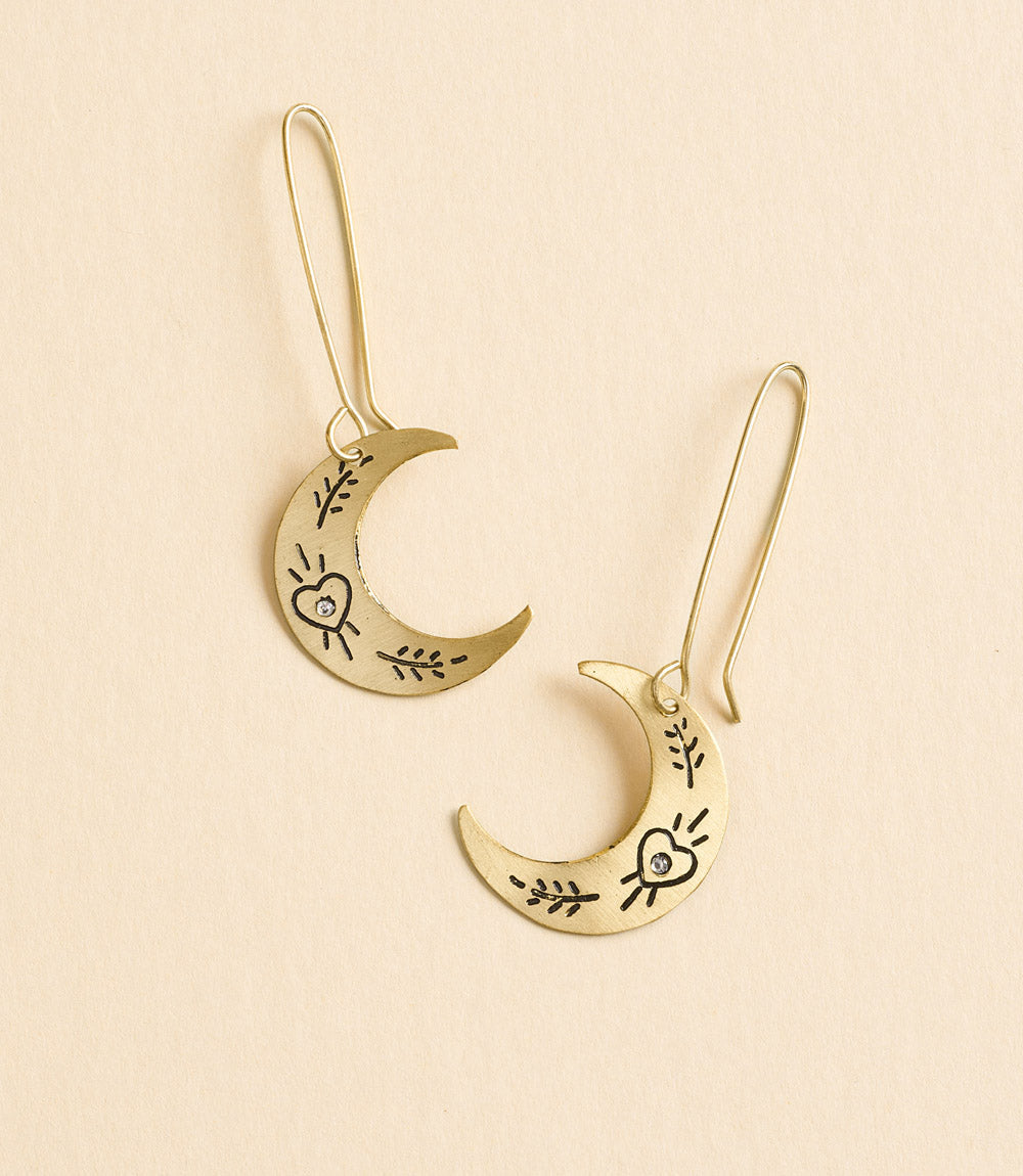 Gold moon-shaped earrings with heart and leaf designs on a beige background