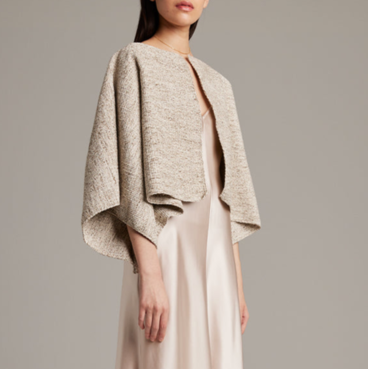 Woman wearing a beige textured jacket over a plain dress on a neutral background