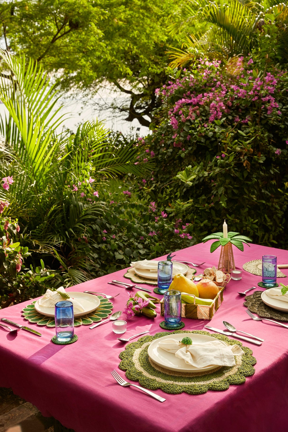 Outdoor dining table setting with pink tablecloth, greenery, and tropical plants.