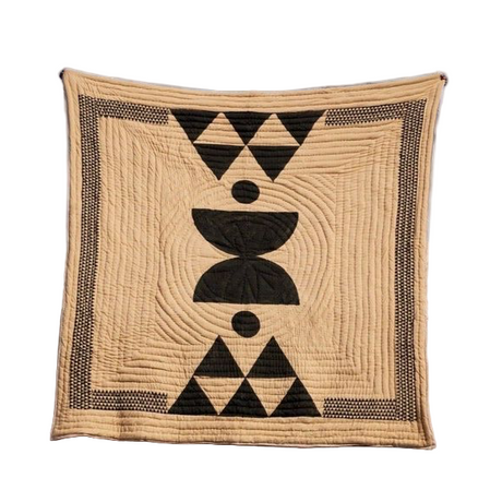 Beige quilt with black geometric patterns on a stone ledge against a blue sky.