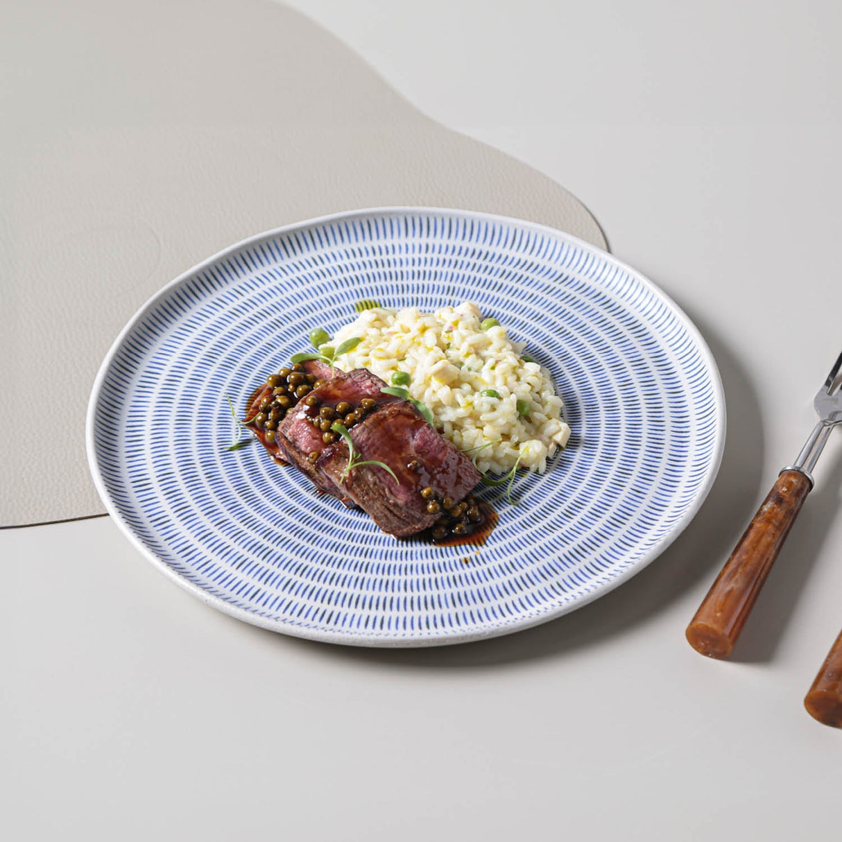 Plated dish with meat and vegetables on a blue patterned plate with cutlery beside it.