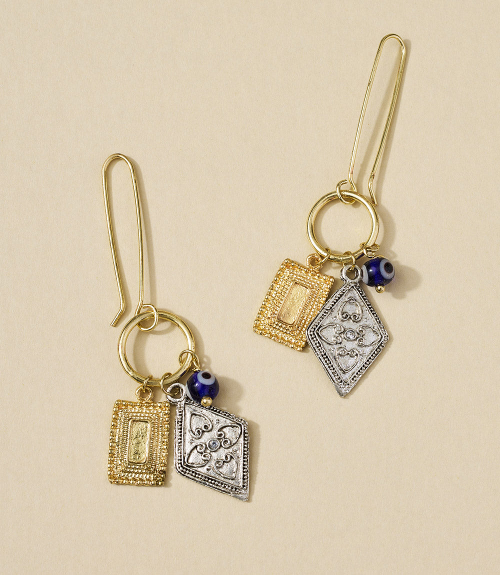 Pair of gold and silver earrings with blue beads on a beige background
