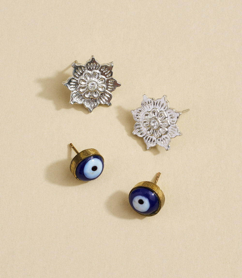 Set of silver floral earrings and gold evil eye earrings on a beige background