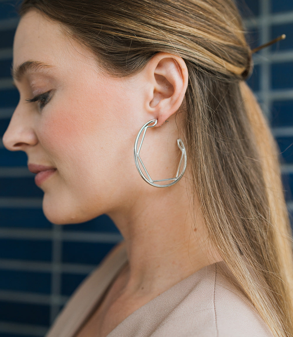 Close-up of a woman wearing silver hoop earrings with a blue tiled background
