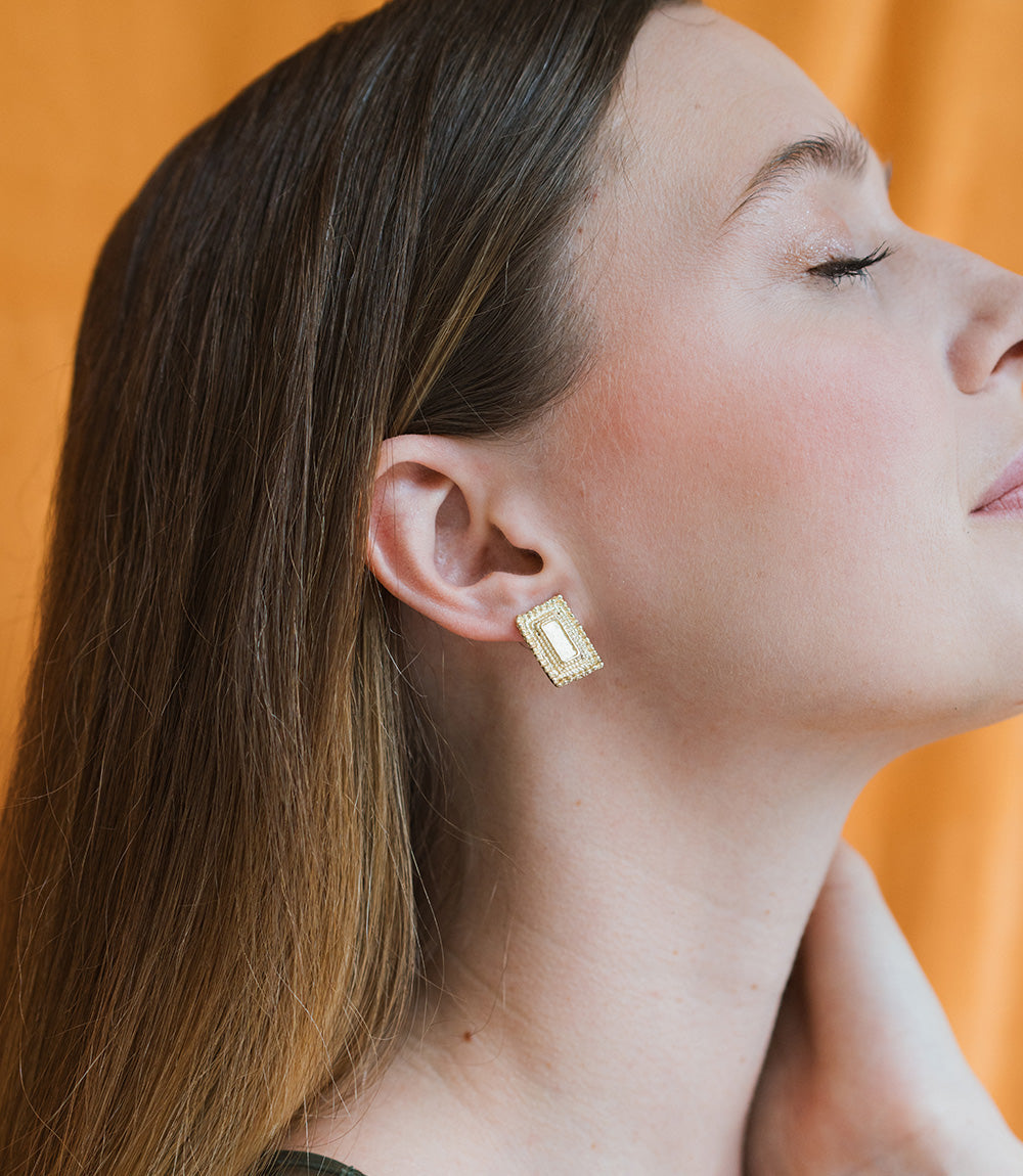 Woman wearing gold earrings against an orange background
