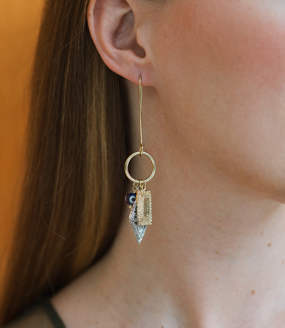 Close-up of an earring with a gemstone hanging from a person's ear against a blurred background.