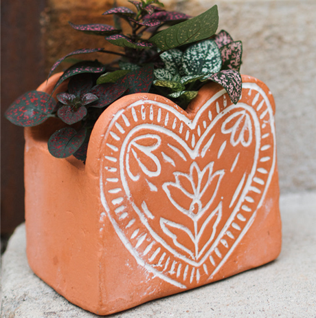 Terracotta heart-shaped planter with decorative patterns and plants on a neutral background