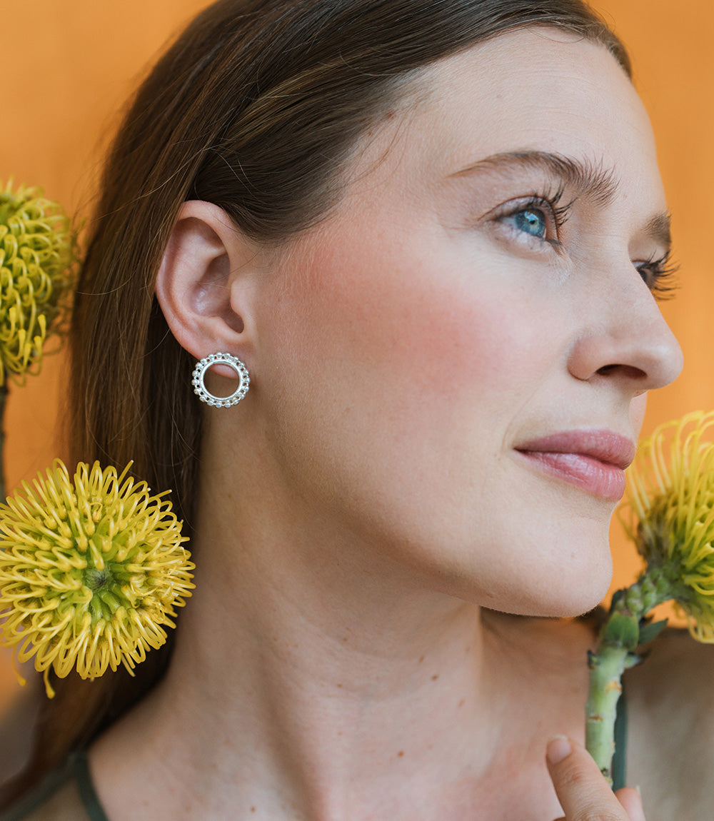 Woman wearing a silver hoop earring with yellow flowers in the background