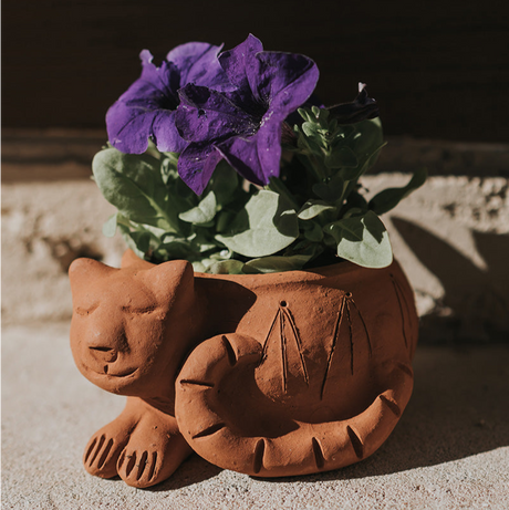 Terra cotta cat-shaped planter with purple flowers on a wooden surface