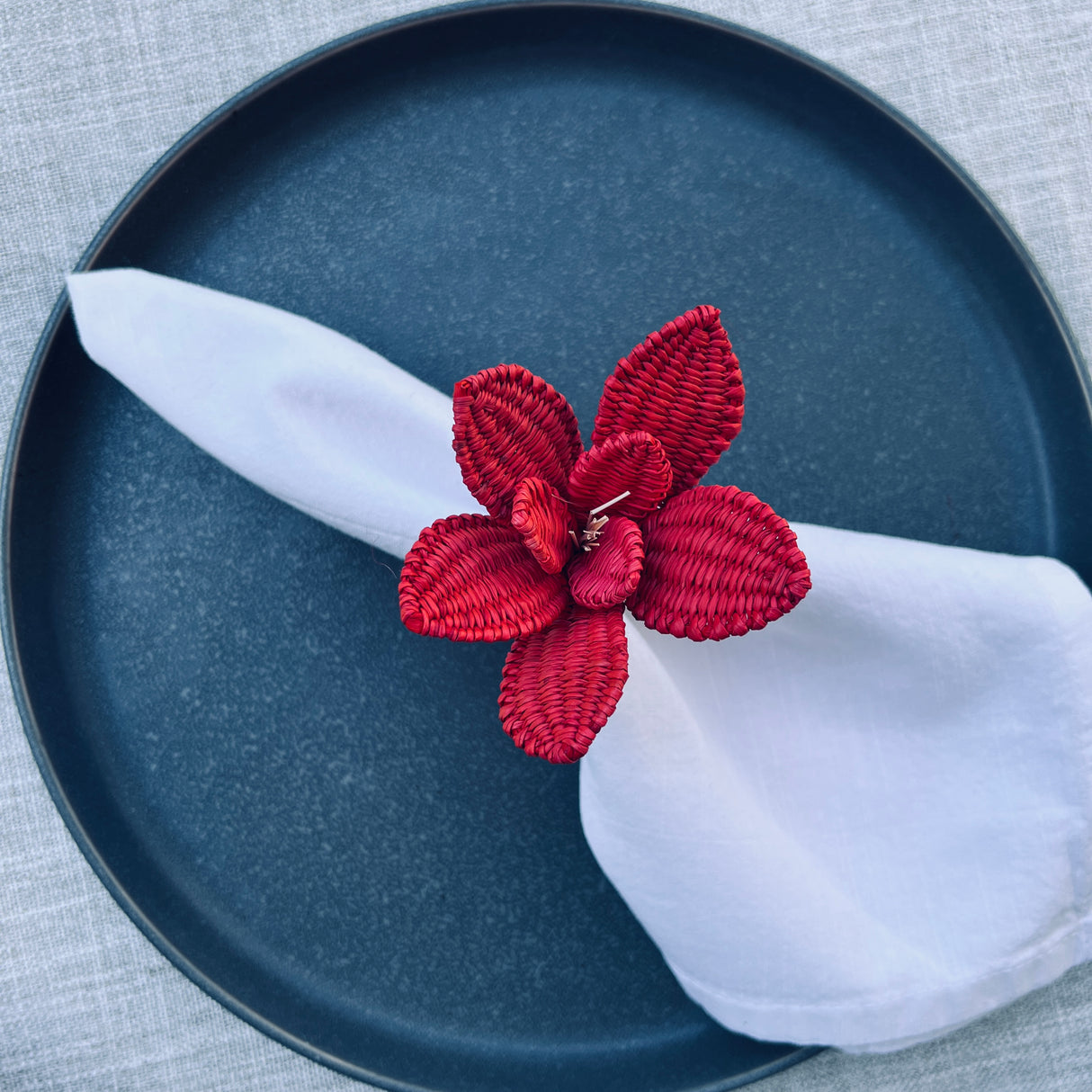 Red floral napkin ring on a white napkin on a blue plate with a gray background
