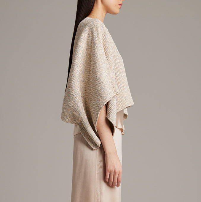 Woman wearing a beige knitted poncho against a plain background