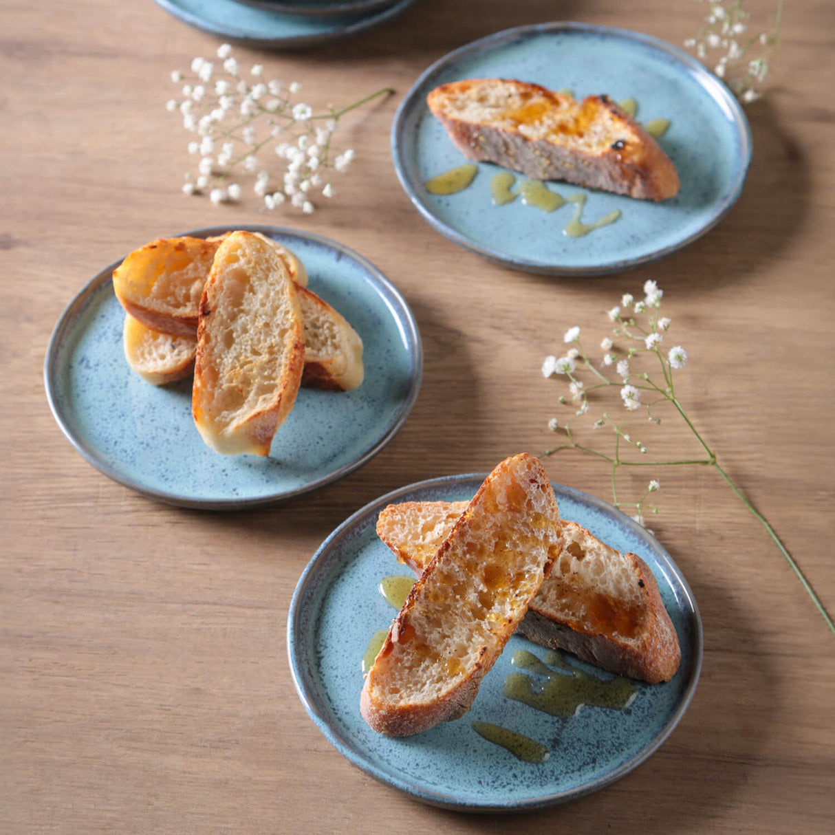 Three blue plates with bread slices on a wooden table with white flowers.