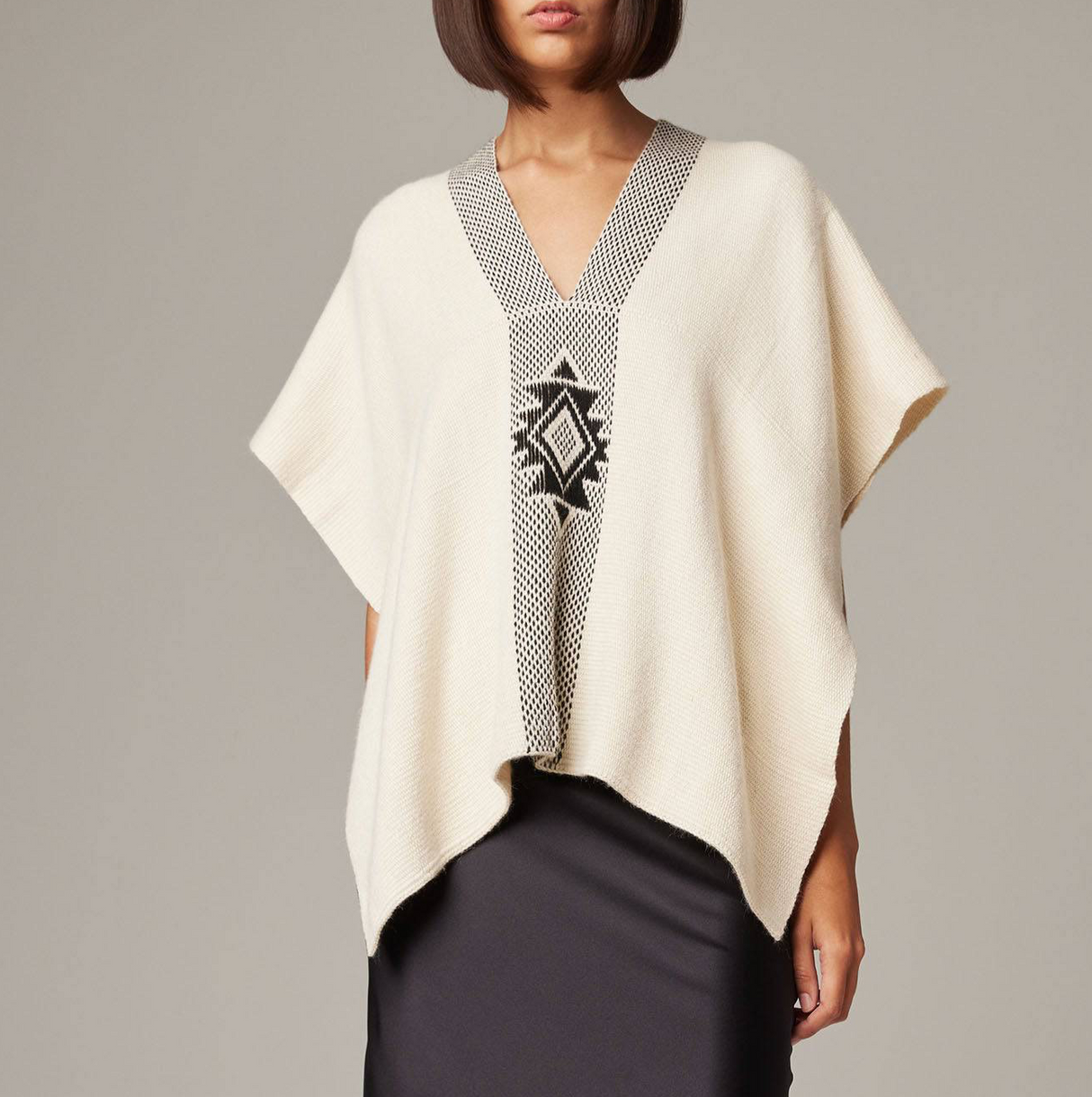 Woman wearing a cream poncho with a patterned front on a gray background