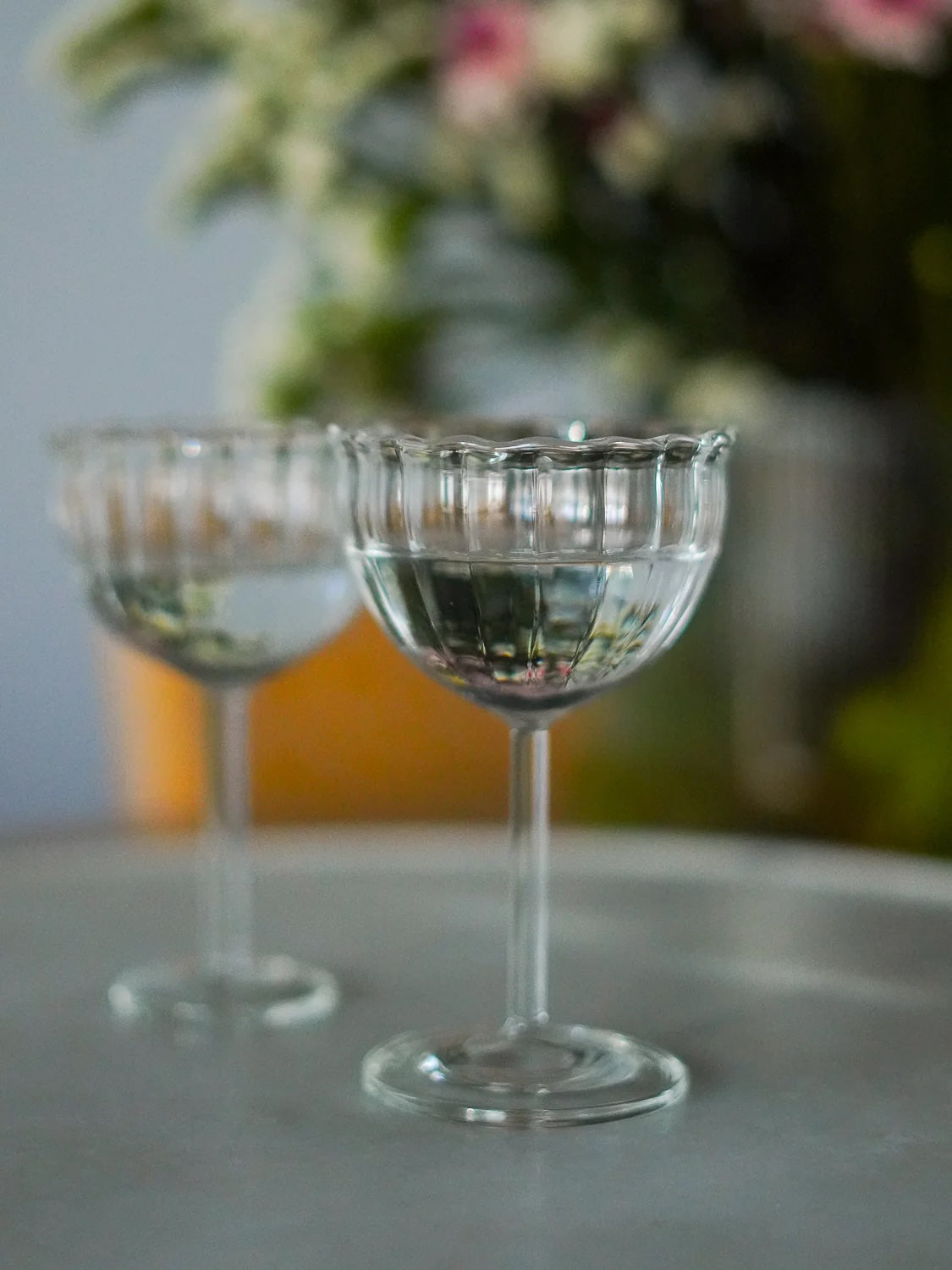 Two glass goblets on a table with a blurred floral background