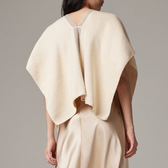 Woman wearing a beige poncho over a plain background