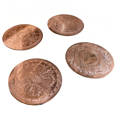 Four copper coasters with intricate designs on a white background