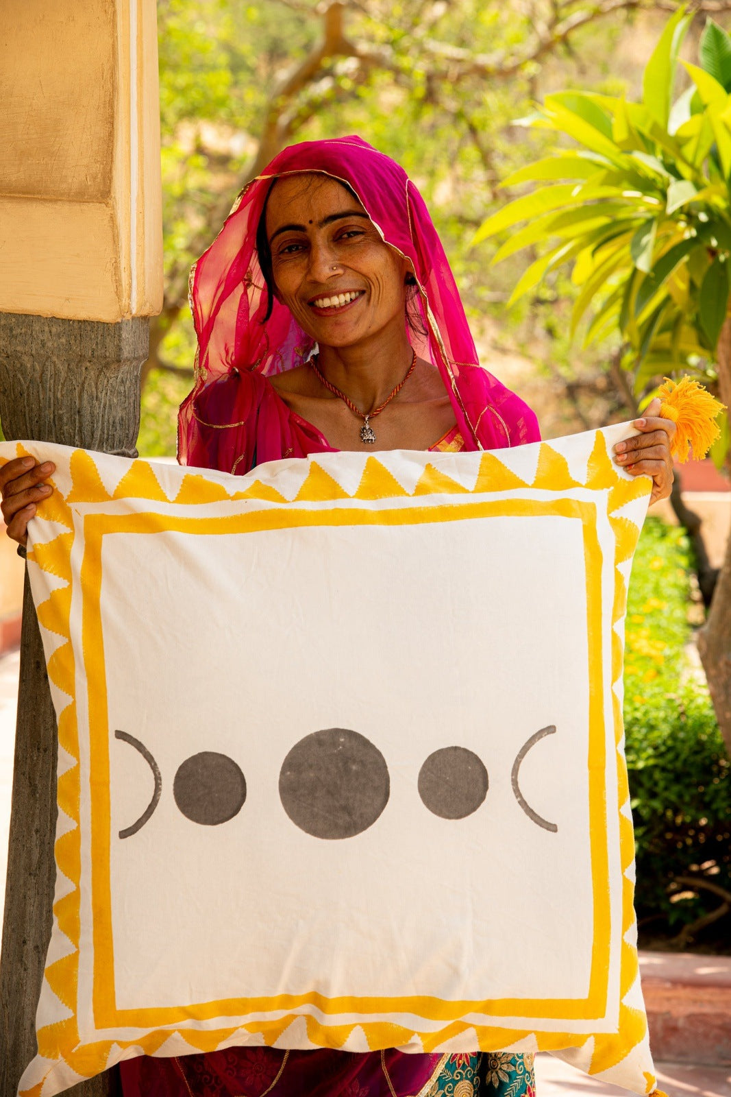Woman holding a decorative pillow with a yellow border and black symbols, outdoors.