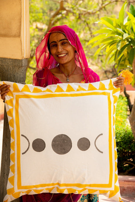 Woman holding a decorative pillow with a yellow border and black symbols, outdoors.